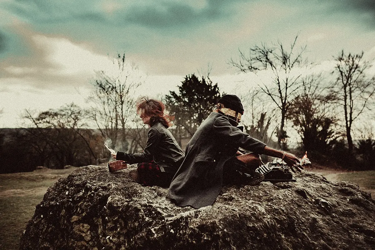 Deux personnes sur photo qui sont dos à dos et assis sur un rocher.