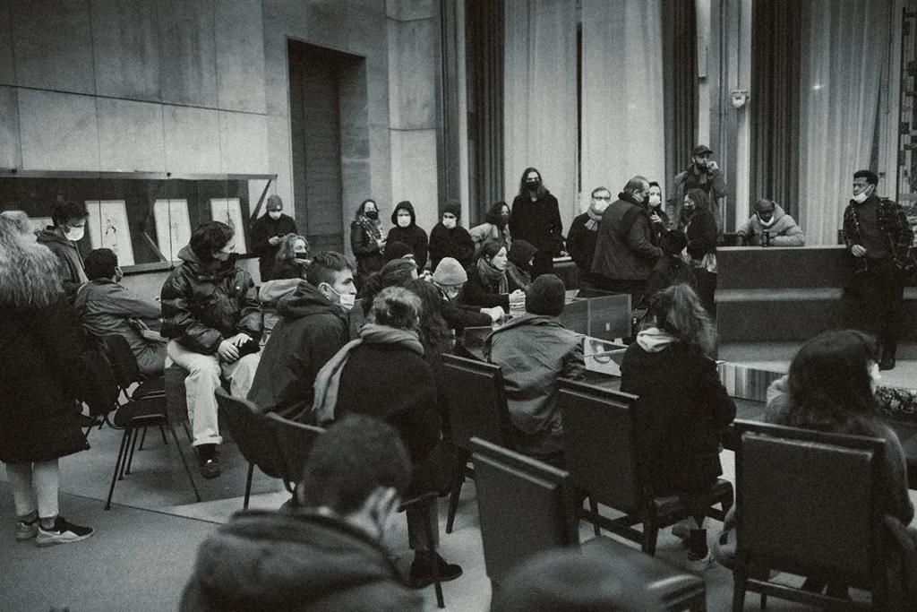 Une autre photo d'un rassemenblement dans une salle avec un groupe de personne qui attendent. La photo est en noir et blanc.