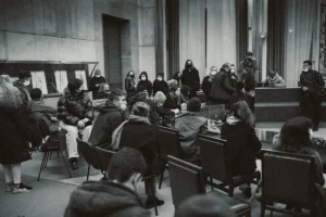 Une autre photo d'un rassemenblement dans une salle avec un groupe de personne qui attendent. La photo est en noir et blanc.