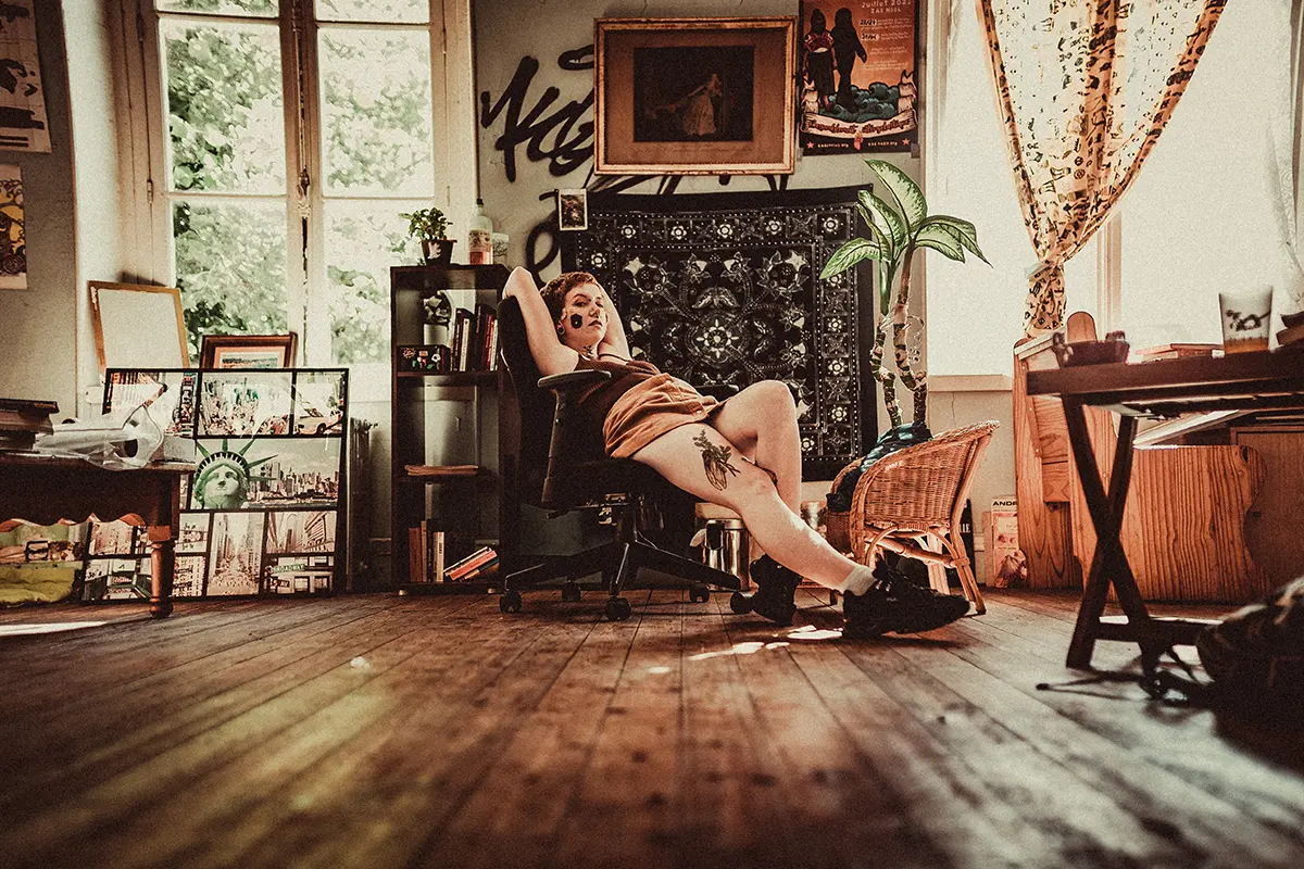 Sur l'image nous pouvons voir un modèle féminin qui pose allonger sur une chaise dans un salon avec le regard vers l'objectif du photographe.