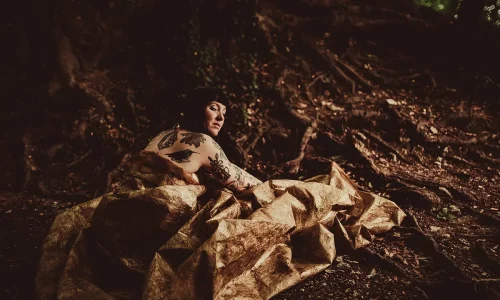 Une jeune femme est à moitié nue dans la forêt. Elle est recouverte d'une couverture.